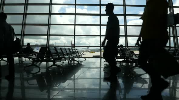 Travelers Walking Along Window in Airport Terminal, People Silhouettes Walking.