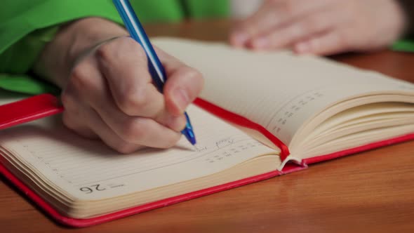 Woman Writes Schedule of Work in Diary Sitting at Table