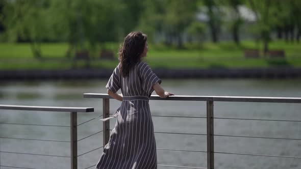 the Brunette in a Striped Dress Stands By the River on a Sunny Day