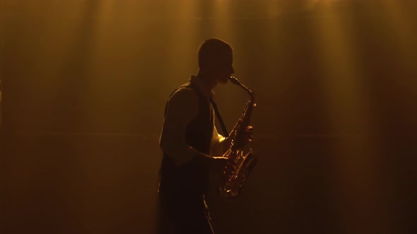 Silhouette a Young Stylish Guy Plays the Golden Shiny Saxophone in the Yellow Spotlights on Stage