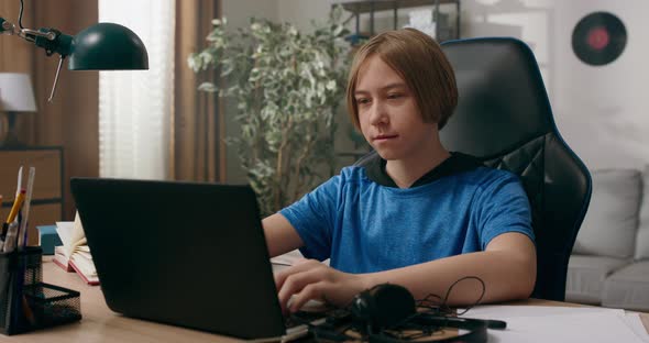 Smart Young Boy Doing Homework in Exercise Book on Laptop