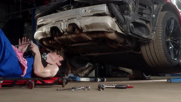 Woman Mechanic in Car Service Take Wrench and Rolls Under Sports Car and Repairs It