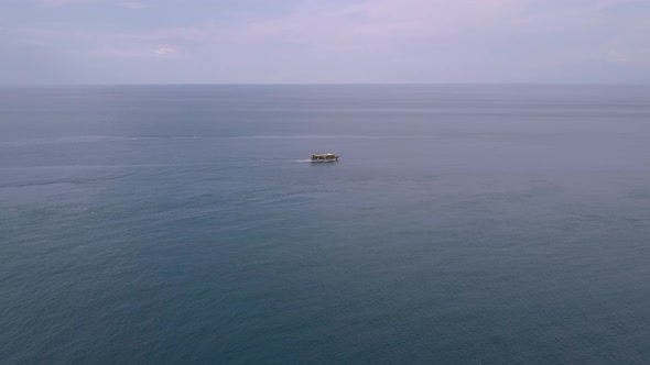 Drone Footage: Tourist Boat Ascending in the Serene Blue Ocean Towards Horizon.