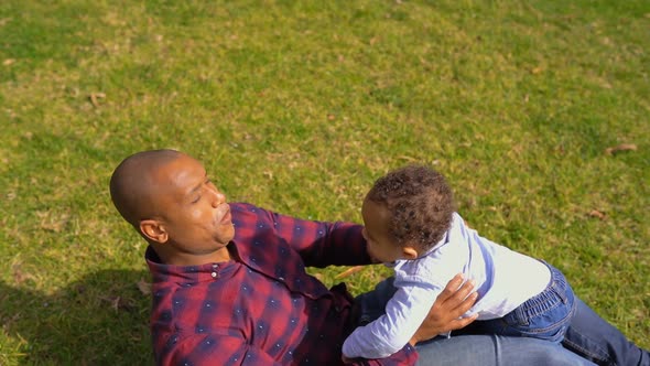 Little Boy Playing with His Father Lying on Grass in Park