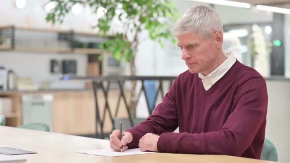 Upset Middle Aged Man Trying to Write at Work Paperwork