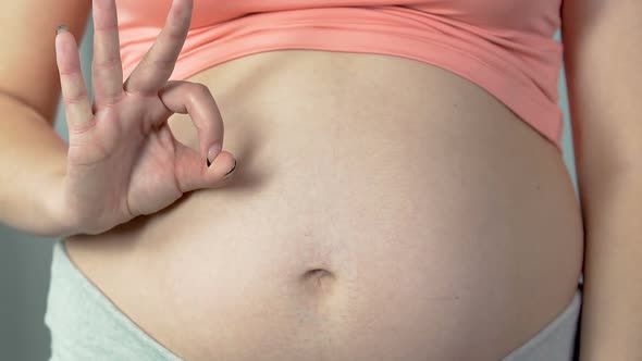 Woman pregnant with child showing okay sign and rubbing belly, healthy pregnancy