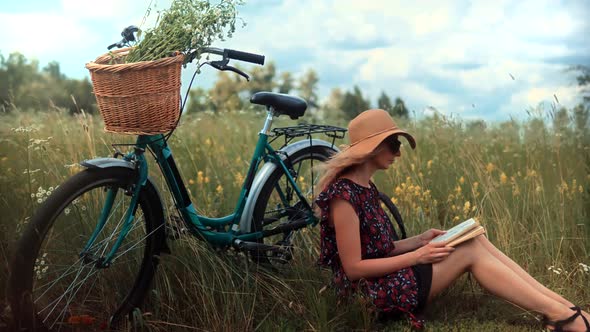 Woman In Dress Relaxing. Woman Sitting On Flower Meadow And Reading Book Diary. Girl On Weekend.