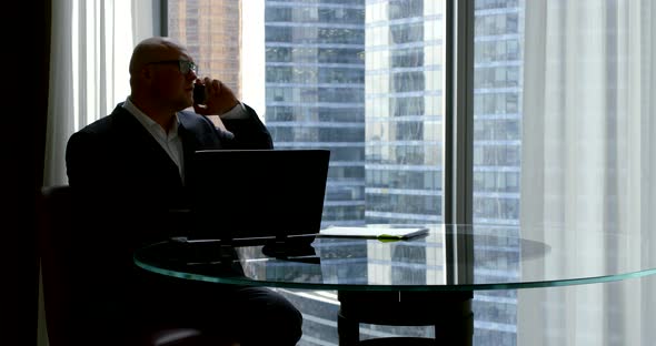 a Businessman in a Business Suit, He Sits in the Office at the Panoramic Window in Which You Can See