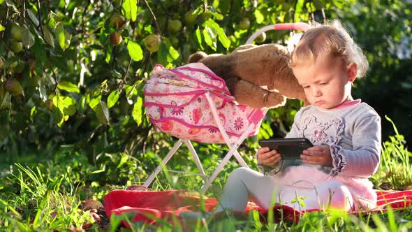 European Child Playing Near the Stroller She is Sitting on the Green Grass in the Garden