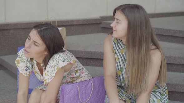 Two Cute Girlfriends Sitting on the Stairs After Shopping with Shopping Bags