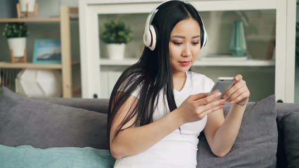 Asian Young Lady with Beautiful Long Black Hair Is Listening To Music Through Headphones and Using