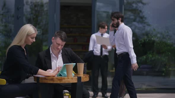 Anxious Caucasian Bearded Man Walking From Side to Side Talking on Phone As Colleagues Working on