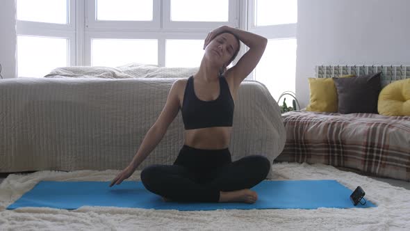 Young Woman Doing Yoga Exercise with Smartphone Sitting with Legs Crossed in Half Lotus Meditating