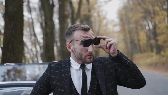 Handsome Gentleman in Suit Stands at Retro Car and Puts on Sunglasses