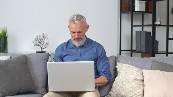 Middleaged Man in Smart Casual Shirt Using Laptop Sitting on the Couch at Home