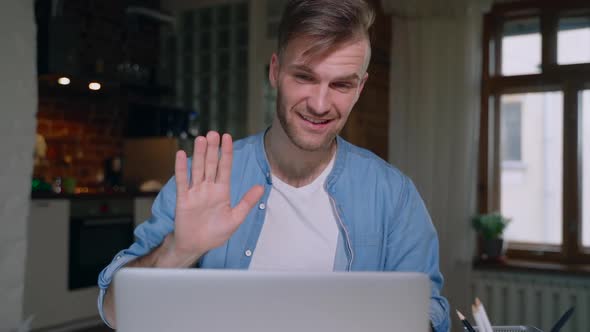 Young American Man is Talking in Video Chat Sitting at Table with Laptop in Apartment Spbas