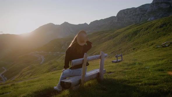 Back view of hipster woman throws his hat up in lights of a sun raises her hands against mountain