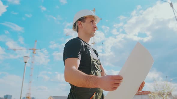 A Man in a Helmet Is Holding a Construction Plan in His Hands