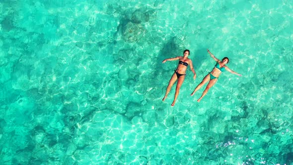 two attractive bikini girls floating and catching sun in the crystal clear turquoise seawater of the