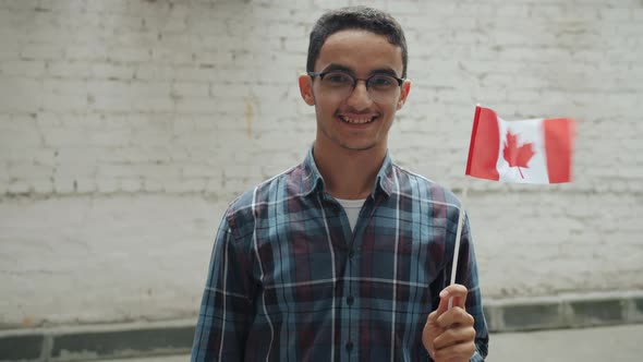 Slow Motion of Middle Eastern Man Waving Canadian Flag and Smiling Standing Against Brick Wall