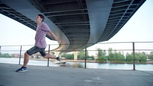 Young Guy Performs a Trick Under the Bridge Parkour in the Ghetto Against the Backdrop of Water