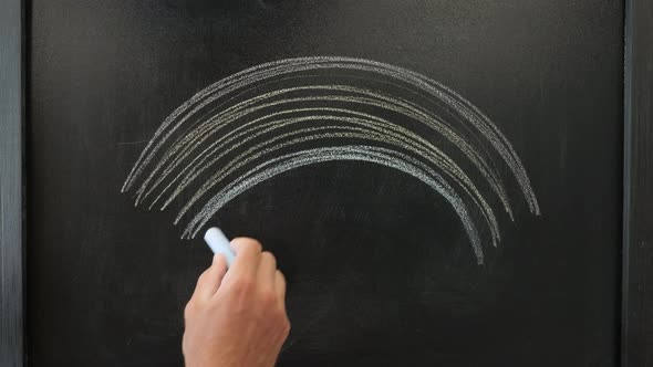 Hand is drawing rainbow with colorful chalks.