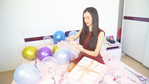 Beautiful Woman with Black Hair Sitting on Bed and Opens Birthday Presents