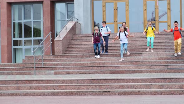 Schoolchildren with Backpacks Run Down Stairs Near School
