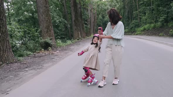 Mother and Daughter in Rollerblades and Helmet Are on the Road in a Park