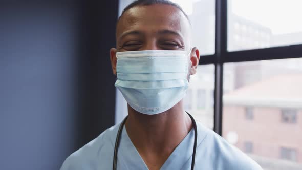 Portrait of mixed race male doctor wearing face mask looking at camera and smiling