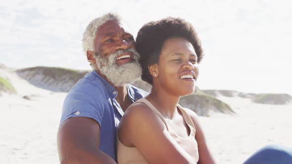 Happy african american couple sitting and embracing on sunny beach