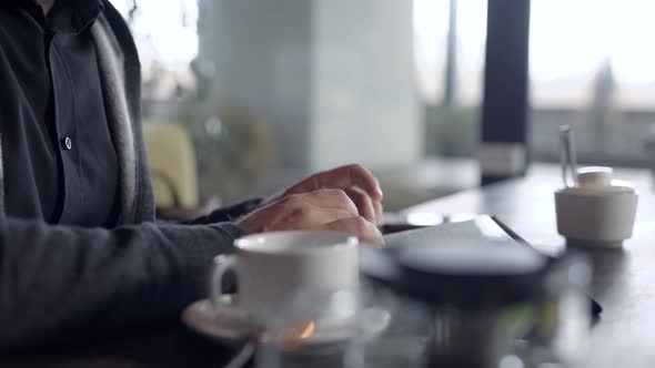 Close-up Shot of a Guy Chatting Online on a Tablet in Cafe, Cup of Tea on Table