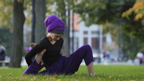 Girl in Hijab Muslim Woman Sports Lady Female Yogi Sitting in City Park on Grass Lawn Holds Foot