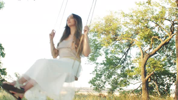 young happy woman swaying rope swing on oak tree,summer leisure at sunset, healthy lifestyle