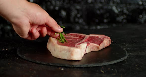 The Men's Hand Puts Rosemary on a Steak Raw Beef T-bone
