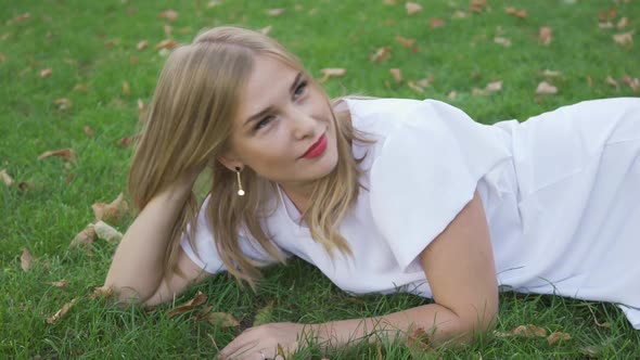 Pretty Blond Woman Lying on the Grass Looking at the Camera and Away Smiling