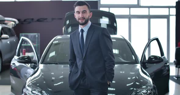 Handsome Young Man Looking Back at New Black Car, Turning To Camera and Smiling. Caucasian