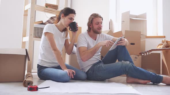 Caucasian Pair Sitting on Floor and Discussing Furnishings in Their New Flat in Slowmotion