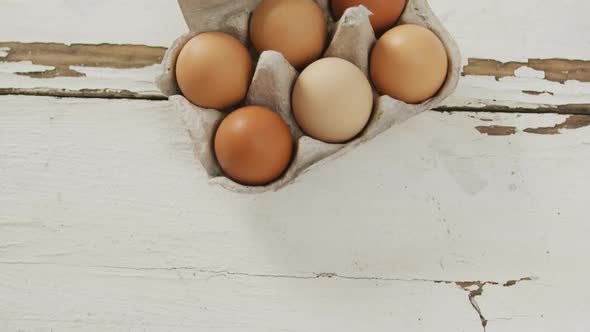 Video of overhead view of brown eggs in egg carton on rustic background