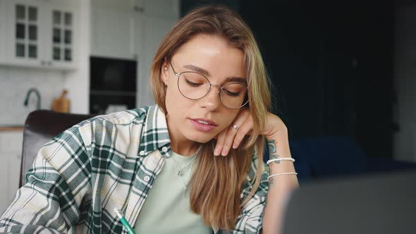 Close Up Portrait of Young Serious Woman Student Watching Webinar Online and Making Notes at Home