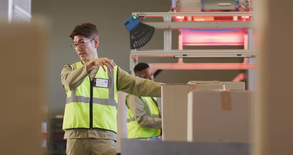 Diverse male workers wearing safety suits with boxes on conveyor belt in warehouse