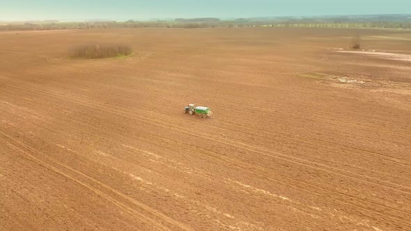 A Red Old Tractor Fertilizes a Green Field in Spring