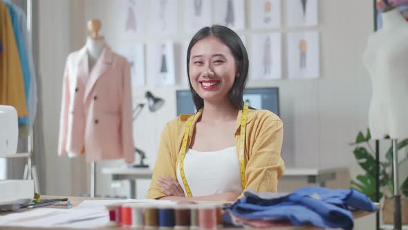 Female Designer With Measuring Tape Around Her Neck Smiling And Crossing Her Arms To The Camera