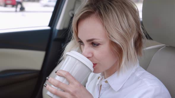 Portrait of Smiling Business Woman in White Shirt Sitting in the Car and Drinking Coffee