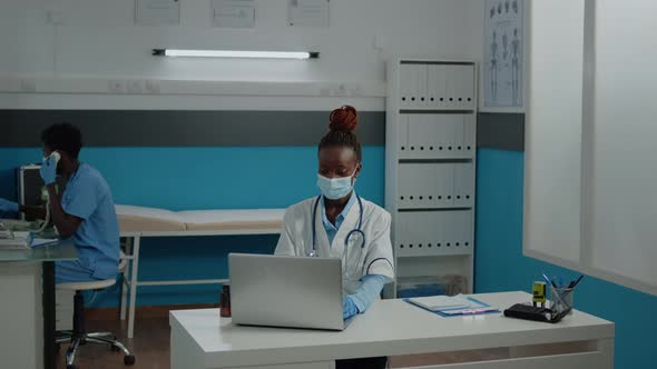 Portrait of African American Doctor Sitting at Desk with Face Mask