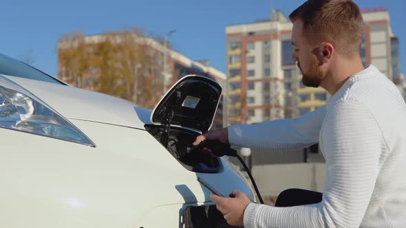 A Fairskinned Male Driver Connects an Electric Car to the Power System to Charge the Car Battery and