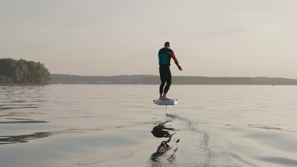 Man Riding on a Hydrofoil Surfboard on Large Lake at Golden Sunset
