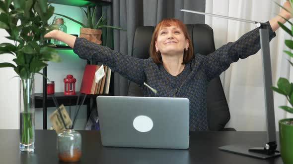 Excited businesswoman is throwing money in office in front of laptop computer