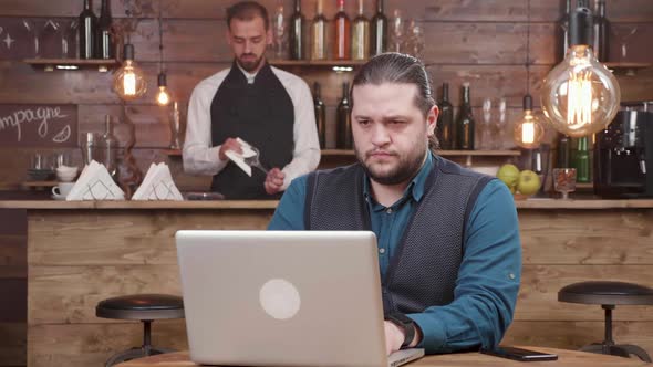 Young Businessman Sitting at a Wooden Table and Working on the Laptop