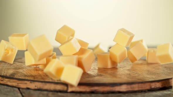 Super Slow Motion Shot of Cheese Chunks Falling on Wooden Board 